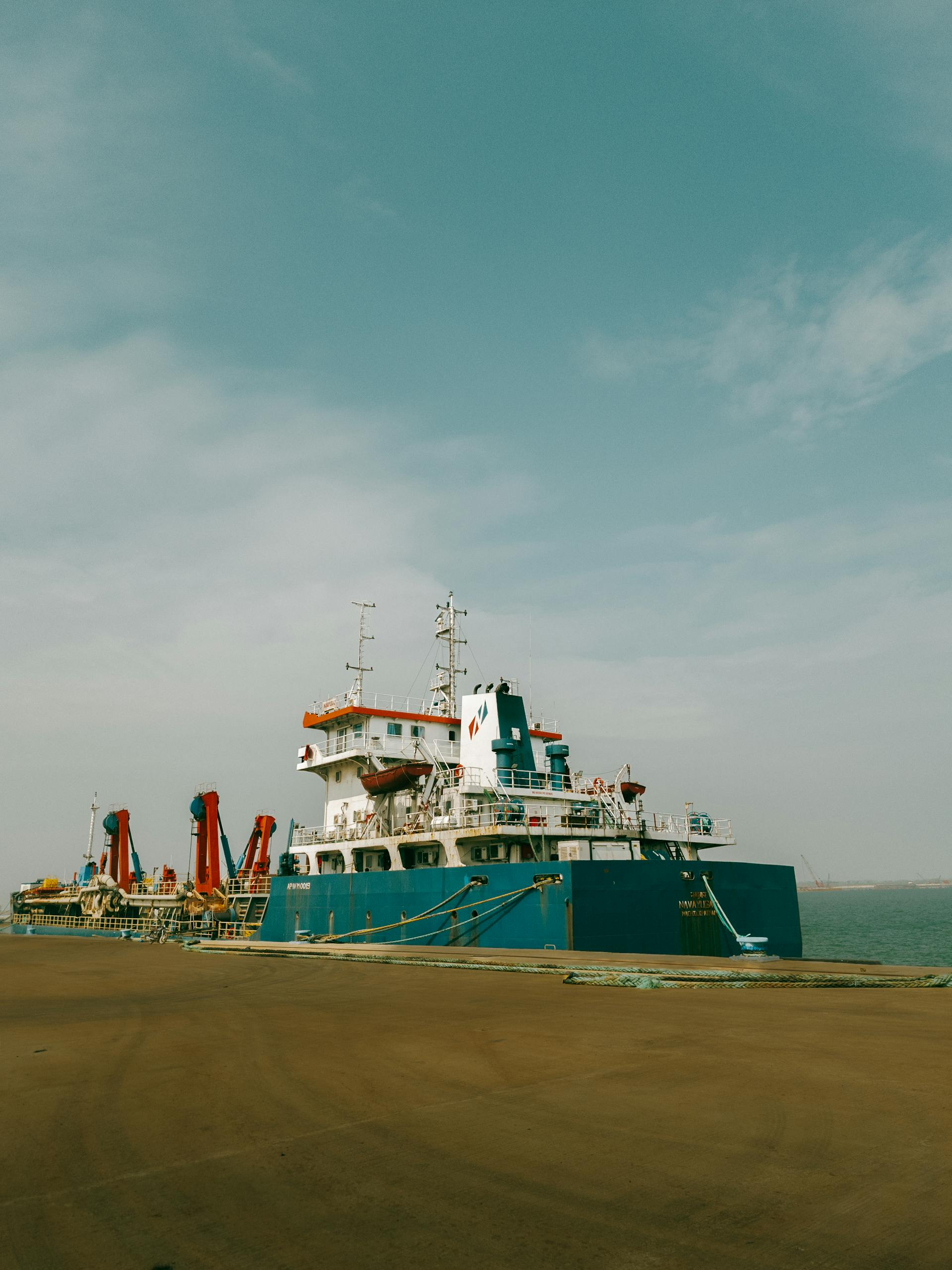 Spacious blue cargo ship moored at a harbor dock against a clear sky.