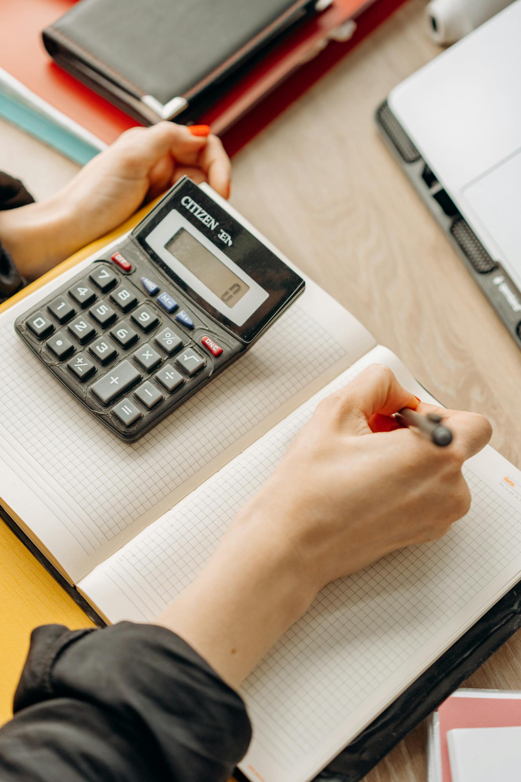 Person writing in notebook with calculator nearby on a desk. Ideal for business or finance themes.