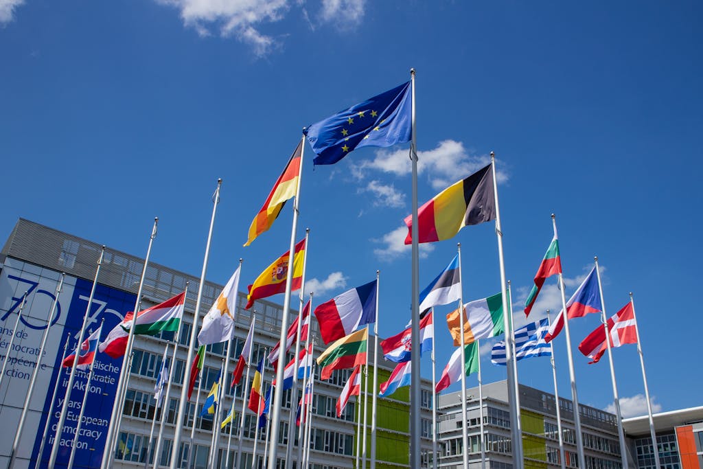 Low angle view of European Union flags on flagpoles against a blue sky, symbolizing unity.